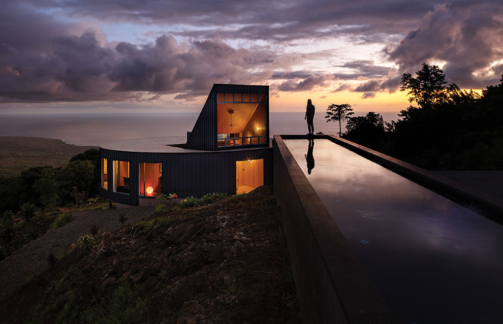 a person standing on a ledge of a house with a pool in front of the ocean