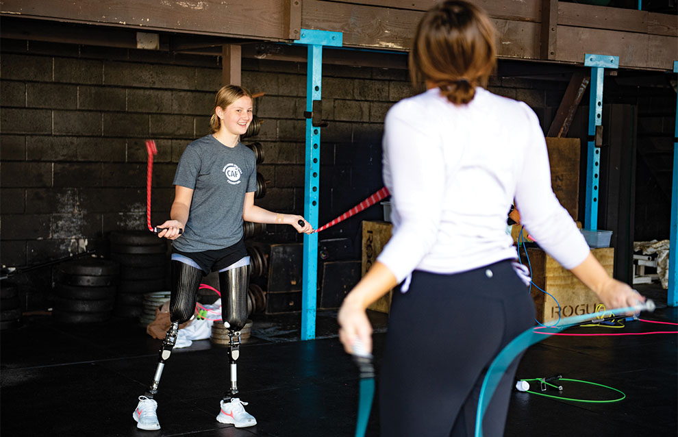 girl with two prosthetic legs trains at gym with coach.