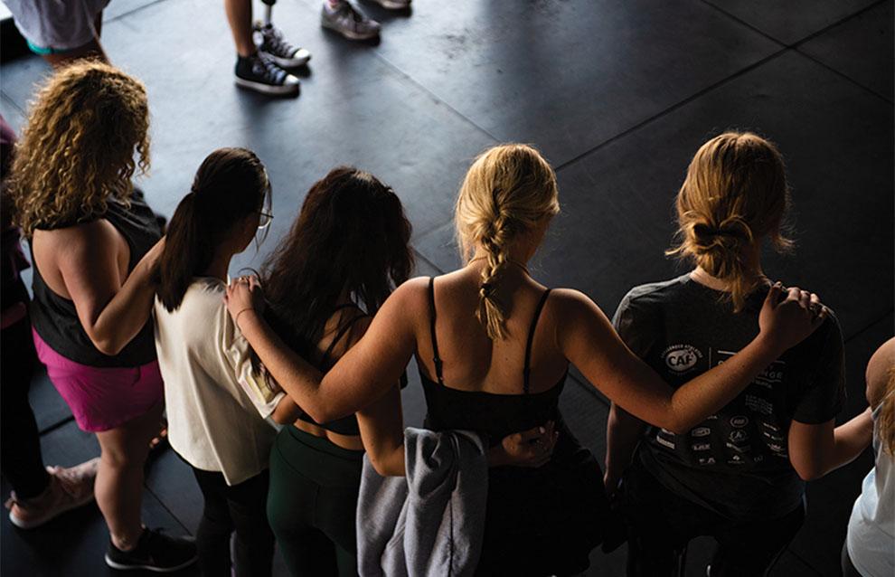 people stand in circle with arms over each other's shoulders in prayer.