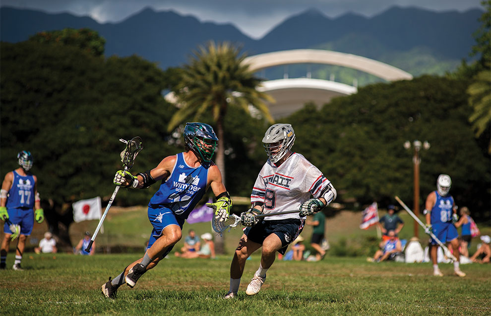 lacrosse players from opposing sides, one in blue jerseys and one in white, in action.
