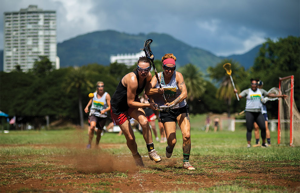 women's lacrosse players kicking up dirt as they run on the field during a game.