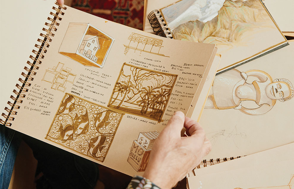 hands opening artist's sketchbook with sketches on the table.