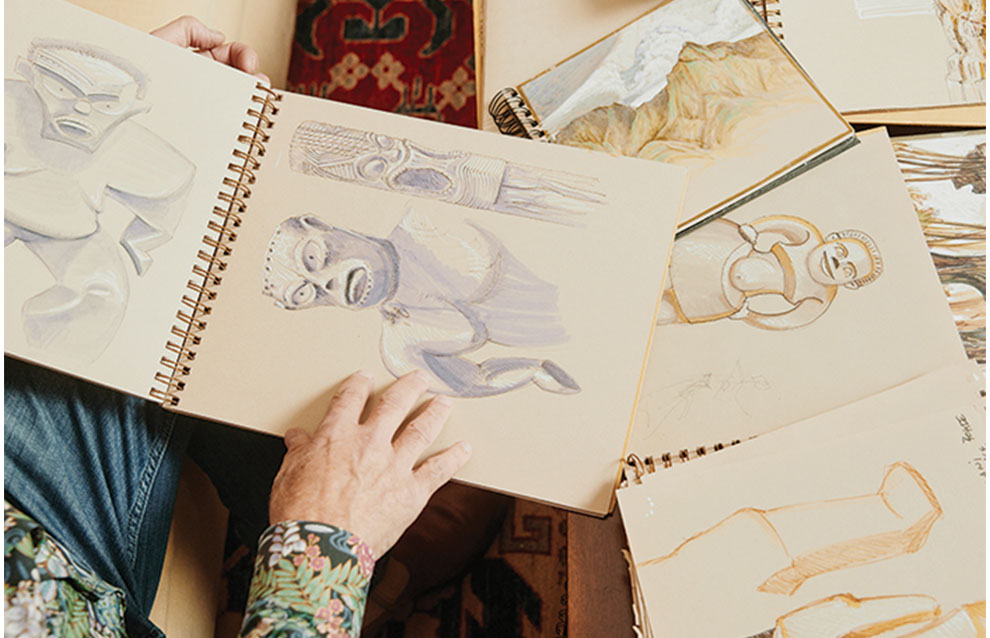 sketches in light pastel colored pencil from multiple sketchbooks scattered on table.