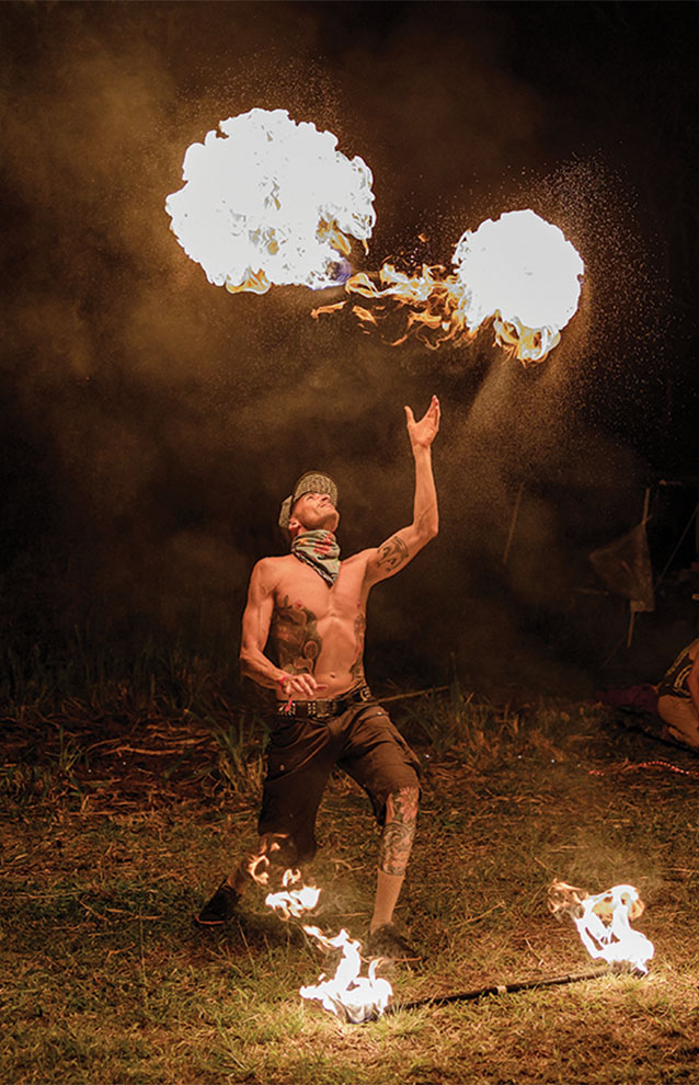 flame thrower tosses lit fire baton in air at night.
