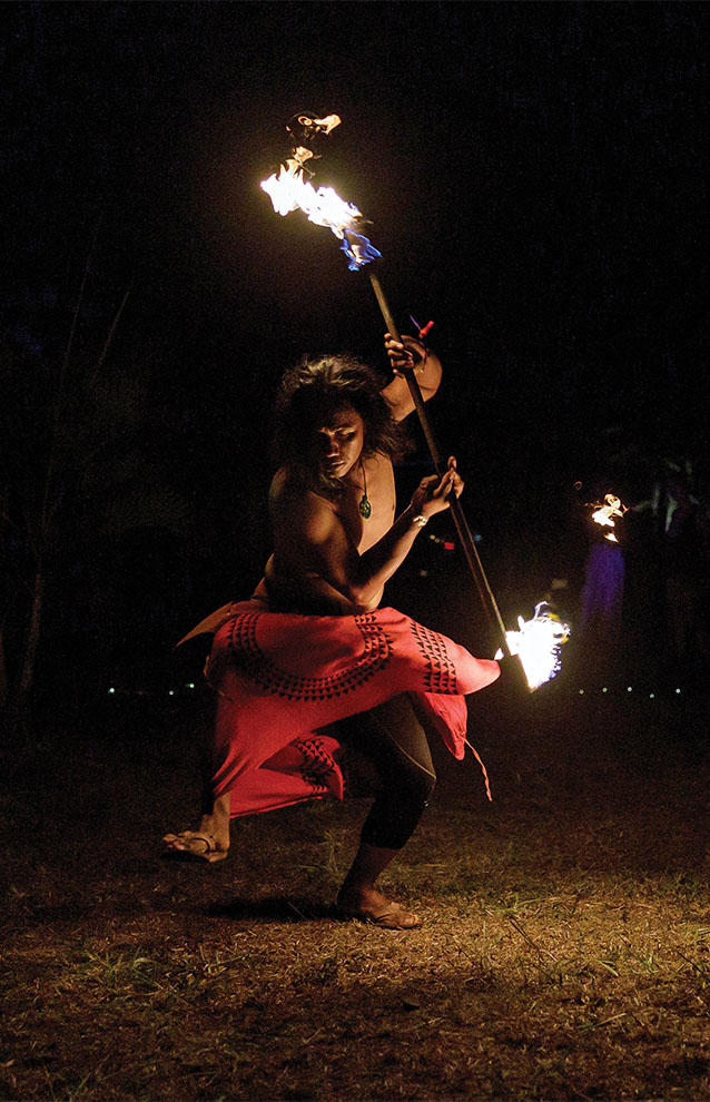 fire performer twirling batons in a red skirt at night.