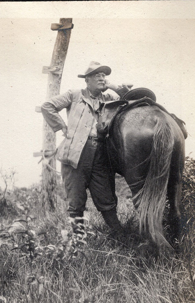black and white photo of man in cowboy hat standing against his horse.